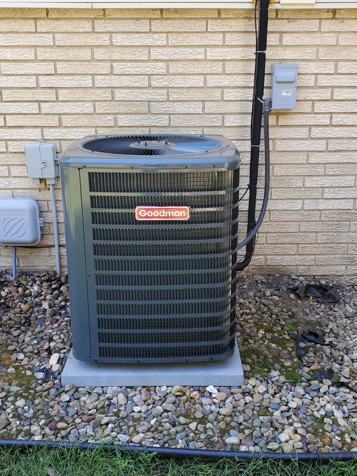 Goodman AC condenser on a pad beside a brick house