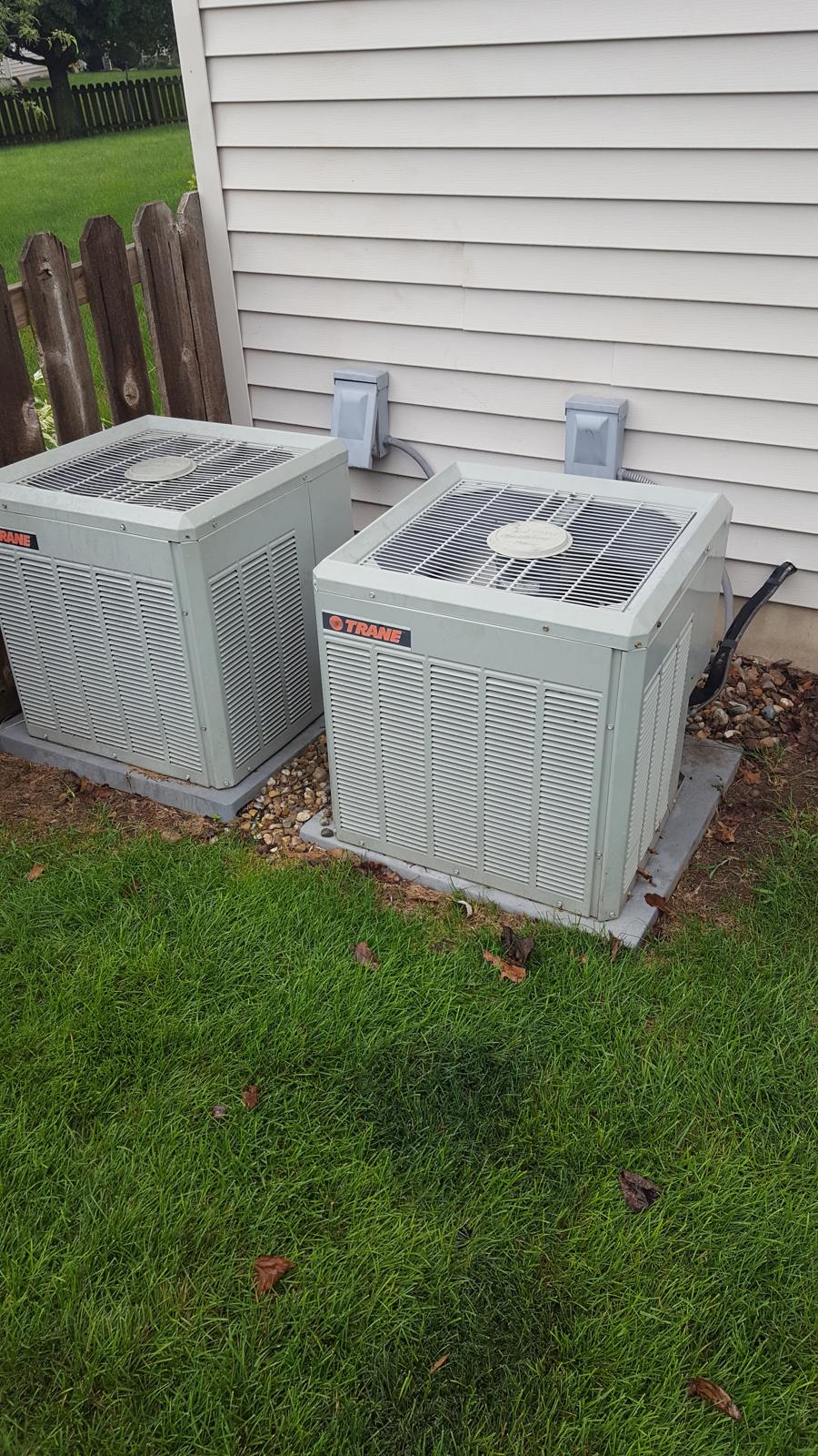 Two air conditioning condensers side by side on a lawn